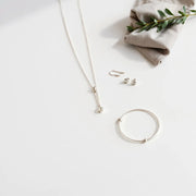 Minimal silver pendant necklace, slim bracelet, and small stud earrings arranged on a light neutral surface