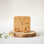 Delicate women’s gold necklace, hoops, ring, and bracelet arranged on a wooden surface in warm daylight