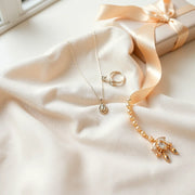 Delicate necklace, earrings, bracelet, and ring arranged on neutral fabric with a satin ribbon nearby