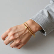 Man’s wrist wearing sleek gold bracelets with a subtle layered chain look on a neutral background