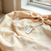Delicate personalized necklace and bracelet on neutral fabric with a ribbon and blank tag
