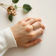 Stacked minimal gold rings on a hand with soft natural light on a neutral background