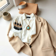 Bold statement earrings, a chunky necklace, and a cuff bracelet styled with a white blouse and beige blazer.