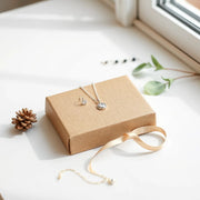Assorted delicate earrings, pendant necklace, and bracelet arranged in a simple gift box with ribbon