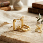Load image into Gallery viewer, Gold hoop earrings on a marble surface with a soft, natural light setting.
