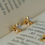Load image into Gallery viewer, Gold star-shaped earrings with clear stones on an open book