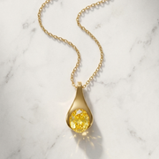 Gold necklace with a yellow gemstone pendant on a marble background