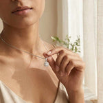 Load image into Gallery viewer, Woman wearing a necklace with a heart pendant in a softly lit room.