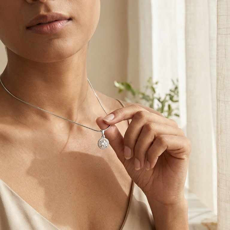 Woman wearing a necklace with a heart pendant in a softly lit room.