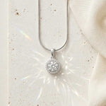 Load image into Gallery viewer, Silver necklace with a round pendant on a white stone surface