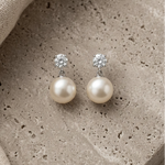 Load image into Gallery viewer, Pair of pearl earrings with clear gemstones on a textured stone surface.