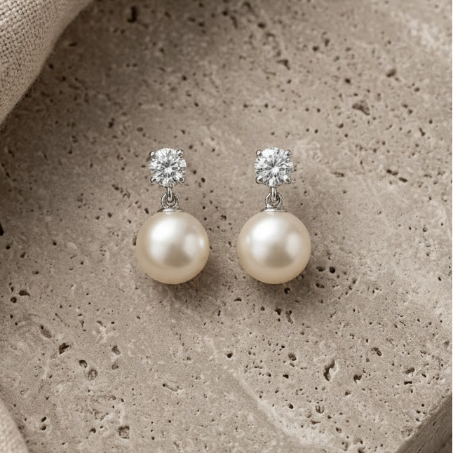 Pair of pearl earrings with clear gemstones on a textured stone surface.