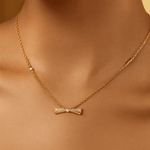 Load image into Gallery viewer, Gold bow-shaped necklace on a person&#39;s neck with a neutral background
