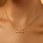 Load image into Gallery viewer, Gold bow-shaped necklace on a person&#39;s neck with a neutral background
